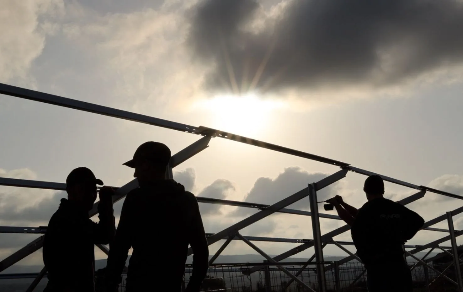 Τεχνικοί συναρμολογούν τη βάση φωτοβολταϊκού συστήματος σε εργοτάξιο υπό το ηλιακό φως – έργο της Axinar