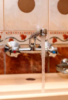 Bathroom faucet with running hot water into sink.