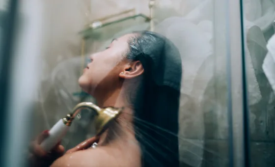 Person taking a hot shower with handheld showerhead, steam on the glass.
