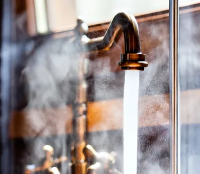 Close-up of running hot water from a brass faucet with steam.